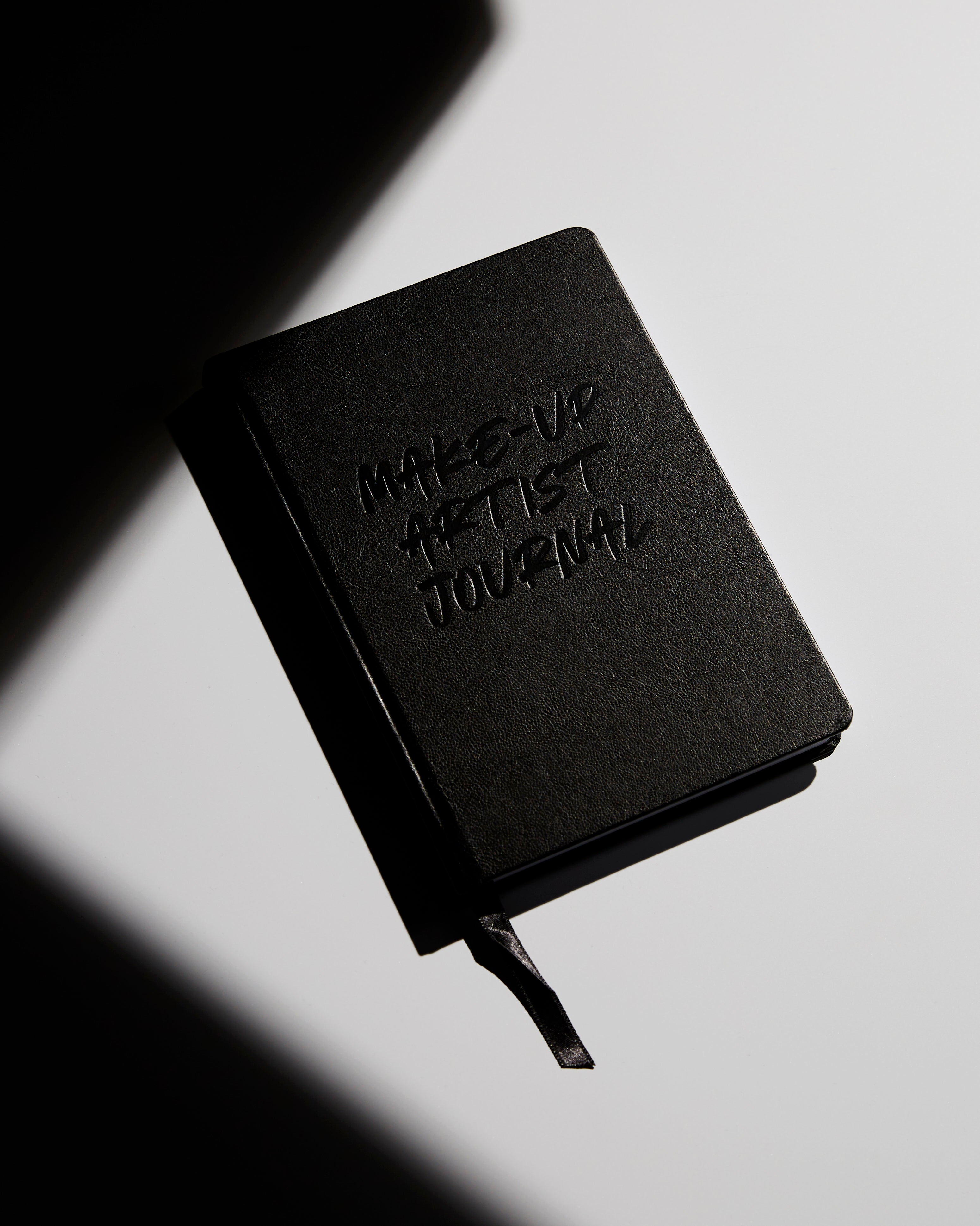A A5 bespoke notebook with black foiling that says Makeup Artist Journal on the cover. The insides pages are all bespoke with the following titles Notes, Face charts, kit list,Feature focus, season review calendar and notes 